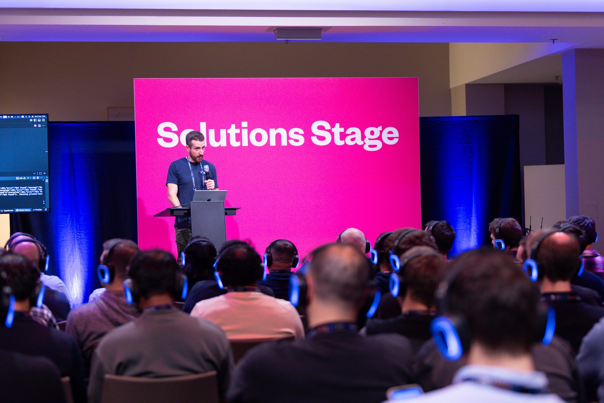 A speaker presenting on the Solutions Stage at LeadDev Berlin, audience wearing silent-disco headphones