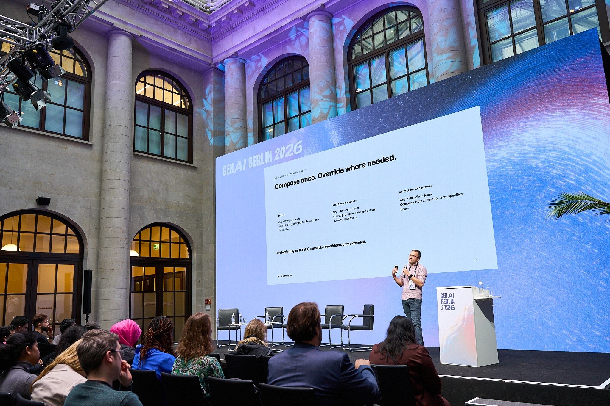 Wide view of the GenAI Berlin 2026 main stage in Humboldt Carré, with Sasa Fajkovic presenting a slide titled “Compose once. Override where needed.”